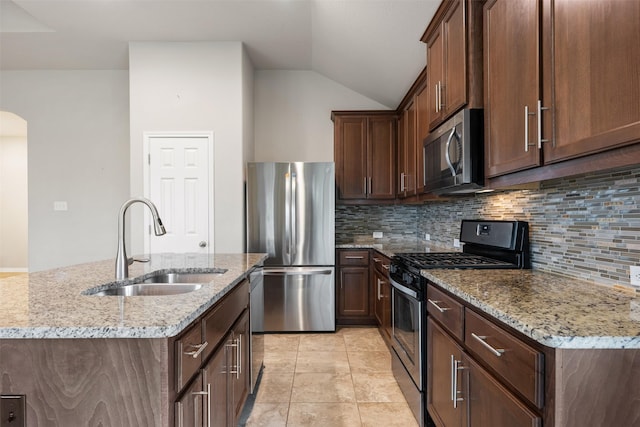 kitchen with sink, stainless steel appliances, light stone counters, and a center island with sink