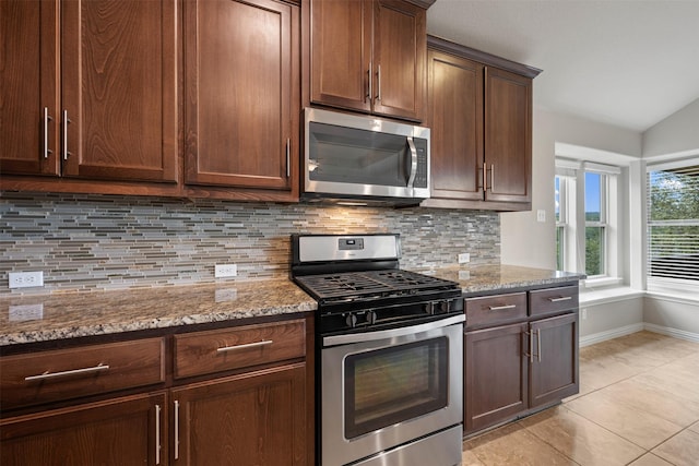 kitchen featuring stainless steel appliances, tasteful backsplash, vaulted ceiling, light stone counters, and light tile patterned floors