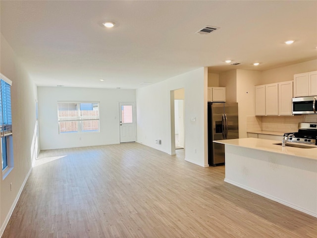 kitchen featuring backsplash, white cabinets, light hardwood / wood-style floors, and appliances with stainless steel finishes