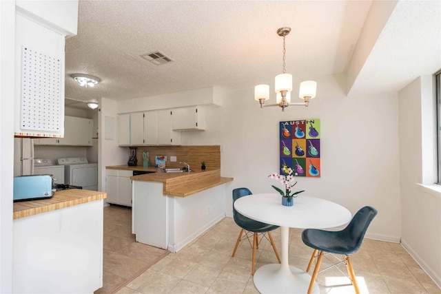 kitchen featuring visible vents, washing machine and clothes dryer, a peninsula, a sink, and light countertops