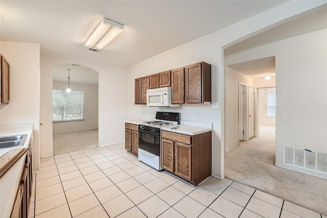 kitchen with gas range oven, light colored carpet, and hanging light fixtures