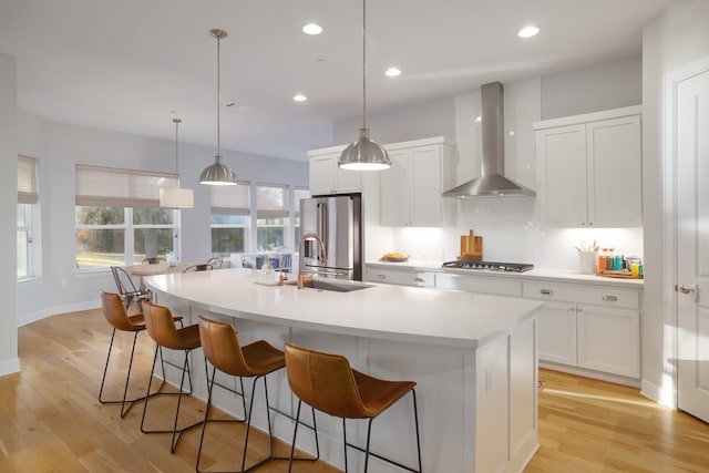 kitchen with wall chimney exhaust hood, sink, a kitchen island with sink, and stainless steel appliances