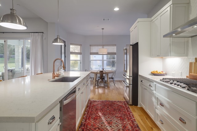 kitchen featuring wall chimney range hood, stainless steel appliances, decorative backsplash, sink, and a kitchen island with sink