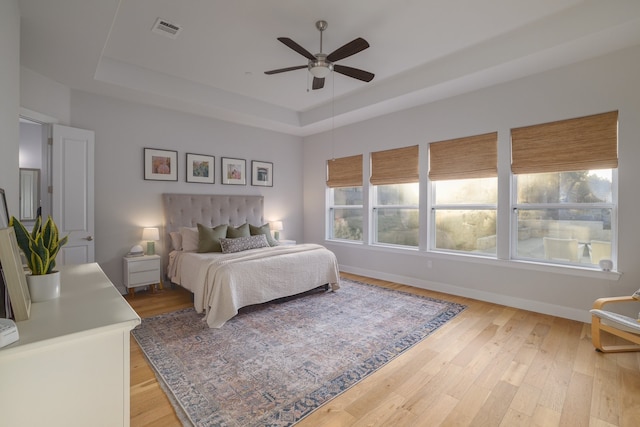 bedroom featuring light wood-type flooring, ceiling fan, and a tray ceiling