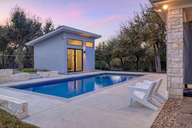 pool at dusk with an outbuilding and a patio