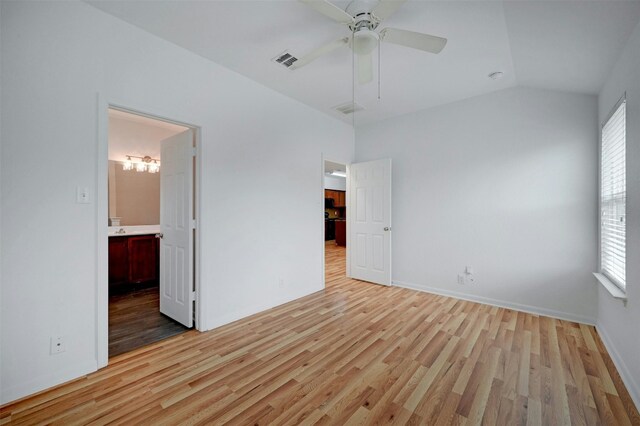 unfurnished bedroom featuring ensuite bathroom, lofted ceiling, light hardwood / wood-style flooring, ceiling fan, and multiple windows