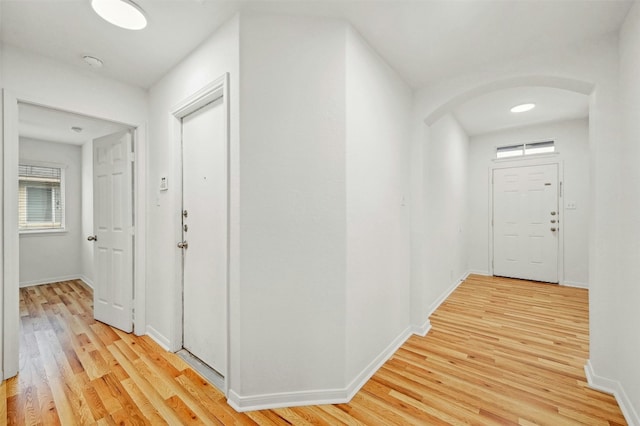 hallway with light wood-style floors, arched walkways, and baseboards