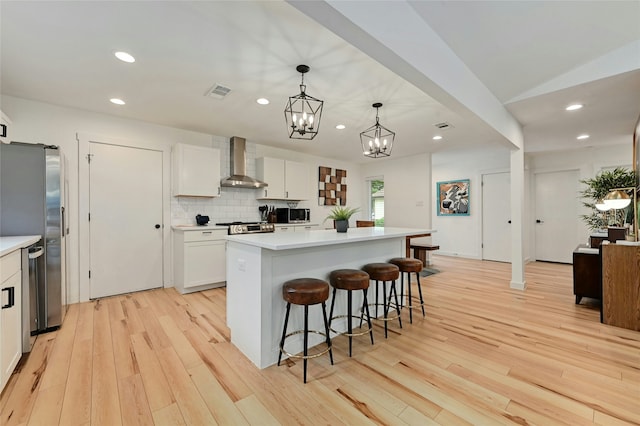 kitchen featuring pendant lighting, a center island, wall chimney exhaust hood, white cabinetry, and stainless steel appliances