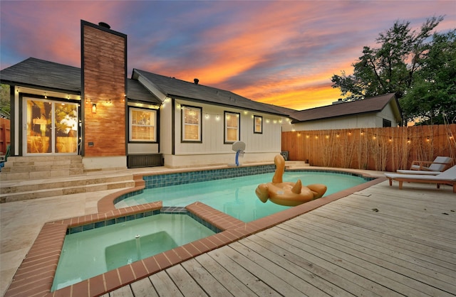 pool at dusk featuring an in ground hot tub and a deck