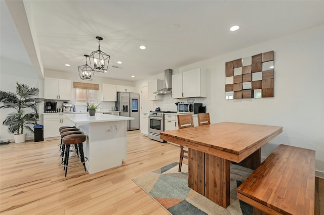 kitchen with wall chimney exhaust hood, white cabinetry, pendant lighting, and stainless steel appliances