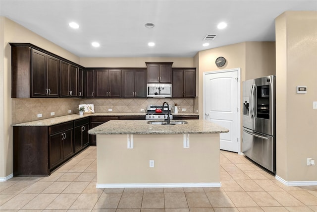 kitchen with stainless steel appliances, light stone counters, a center island with sink, and light tile patterned flooring