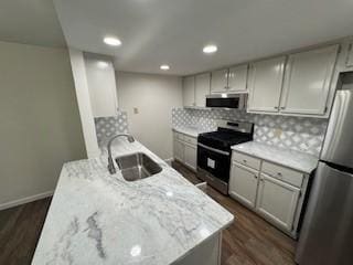 kitchen with sink, dark hardwood / wood-style flooring, backsplash, stainless steel appliances, and light stone counters