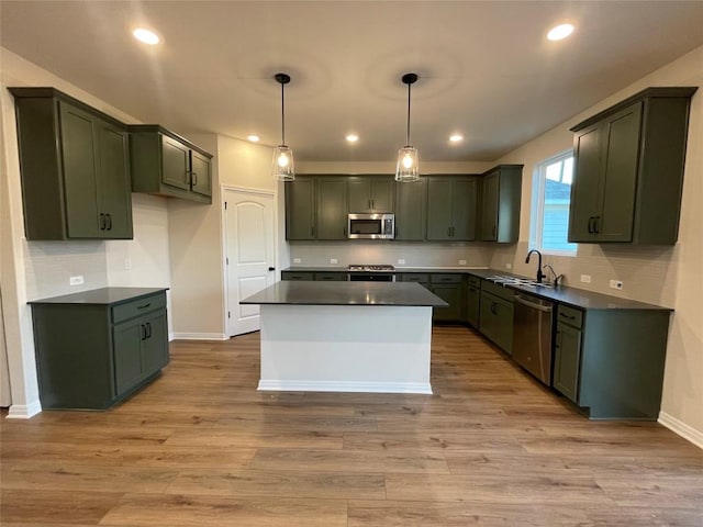 kitchen featuring sink, light wood-type flooring, appliances with stainless steel finishes, green cabinets, and pendant lighting