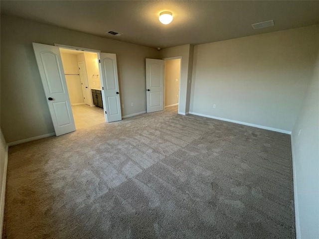 unfurnished bedroom with connected bathroom and light colored carpet