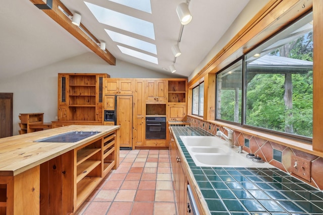 kitchen featuring sink, light tile patterned floors, tile countertops, vaulted ceiling with skylight, and black appliances