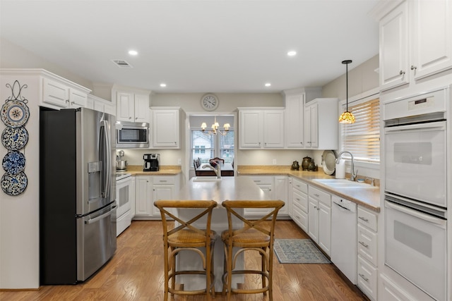 kitchen featuring appliances with stainless steel finishes, sink, decorative light fixtures, white cabinets, and light wood-type flooring