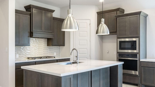 kitchen with appliances with stainless steel finishes, a sink, backsplash, light countertops, and dark brown cabinets