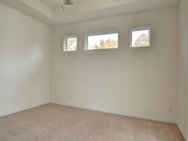 carpeted empty room featuring ceiling fan, a raised ceiling, and plenty of natural light