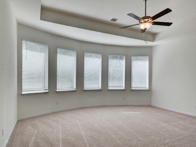 carpeted spare room with a healthy amount of sunlight, ceiling fan, and a raised ceiling