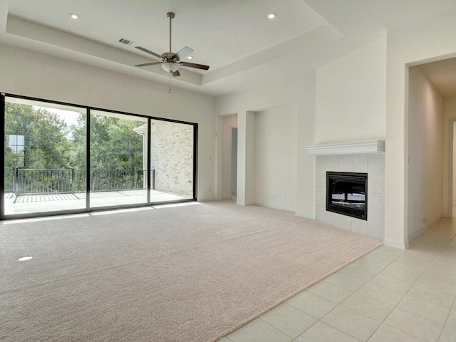 unfurnished living room with a towering ceiling, a tile fireplace, a raised ceiling, ceiling fan, and light tile patterned flooring