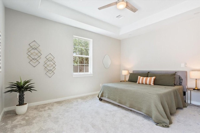 bedroom with light carpet, ceiling fan, and a raised ceiling