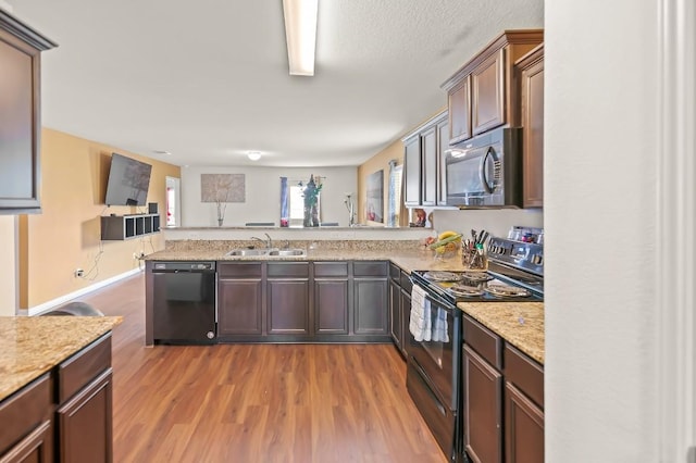 4004 Cressler Ln Unit 10F, Jarrell, TX 76537 - kitchen with black appliances, a peninsula, wood finished floors, open floor plan, and light stone counters