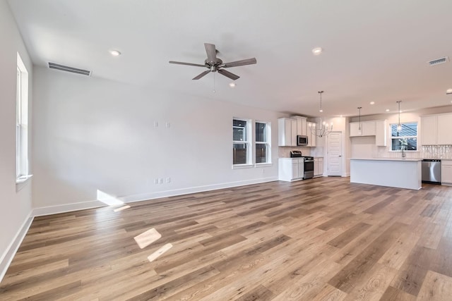 unfurnished living room with ceiling fan with notable chandelier and light wood-type flooring