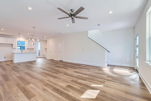 unfurnished living room with ceiling fan with notable chandelier and light hardwood / wood-style flooring