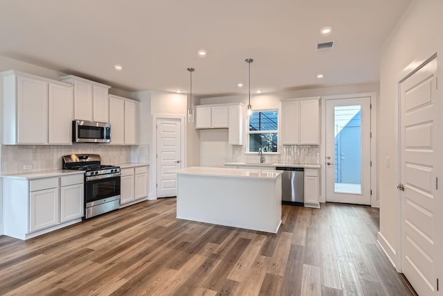 kitchen with hanging light fixtures, white cabinets, hardwood / wood-style floors, a center island, and stainless steel appliances