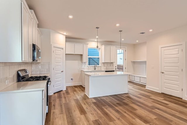 kitchen featuring hanging light fixtures, appliances with stainless steel finishes, sink, white cabinetry, and a center island