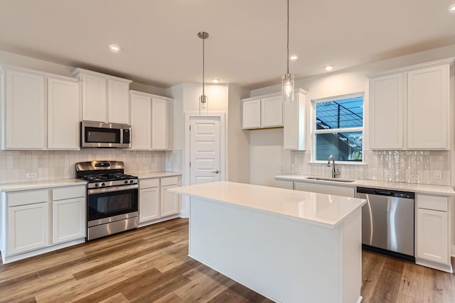 kitchen featuring white cabinets, appliances with stainless steel finishes, a kitchen island, decorative light fixtures, and sink