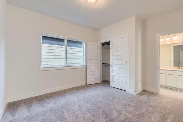 unfurnished bedroom with light carpet, sink, a closet, and ensuite bathroom