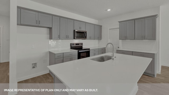 kitchen with range with electric cooktop, gray cabinetry, sink, light wood-type flooring, and an island with sink