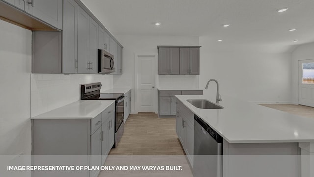 kitchen featuring light hardwood / wood-style flooring, sink, gray cabinetry, decorative backsplash, and stainless steel appliances