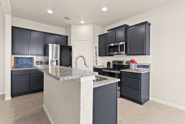 kitchen with light tile patterned floors, appliances with stainless steel finishes, sink, and an island with sink