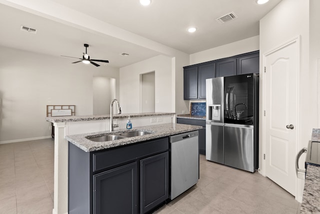 kitchen featuring ceiling fan, appliances with stainless steel finishes, sink, light stone countertops, and a kitchen island with sink