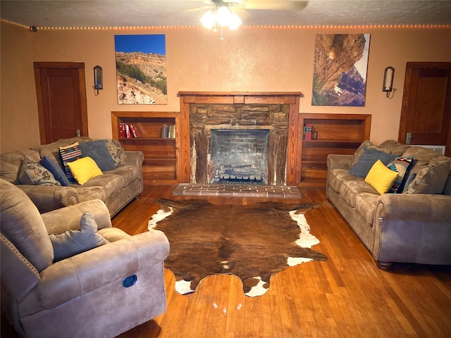 living room with wood-type flooring, built in shelves, ceiling fan, and a fireplace