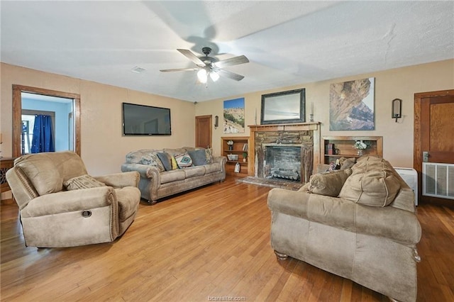 living room featuring ceiling fan, light wood-type flooring, and a stone fireplace