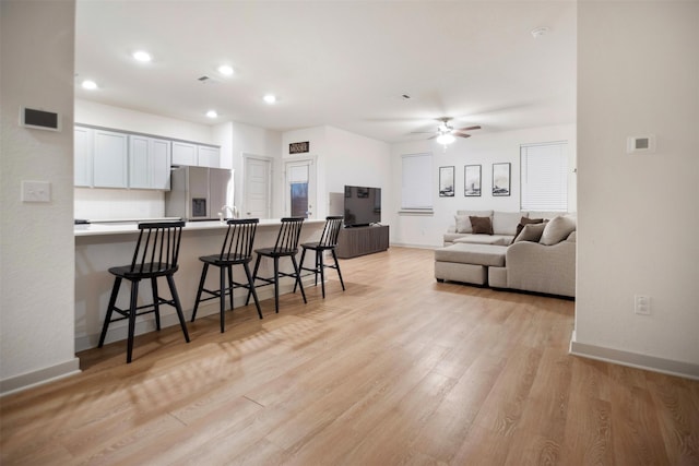 kitchen featuring white cabinets, light hardwood / wood-style flooring, stainless steel refrigerator with ice dispenser, and a kitchen breakfast bar