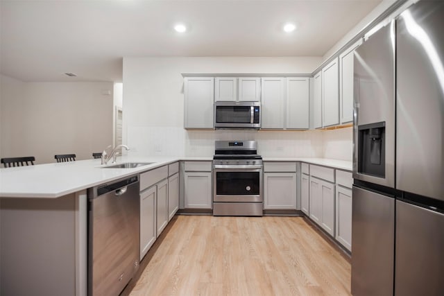 kitchen featuring appliances with stainless steel finishes, a kitchen bar, sink, kitchen peninsula, and light hardwood / wood-style flooring