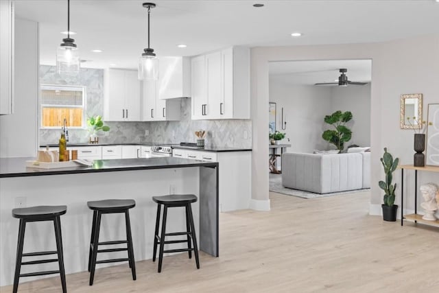 6003 Libyan Dr, Austin, TX 78745 - kitchen with dark countertops, a breakfast bar, white cabinetry, wall chimney range hood, and recessed lighting
