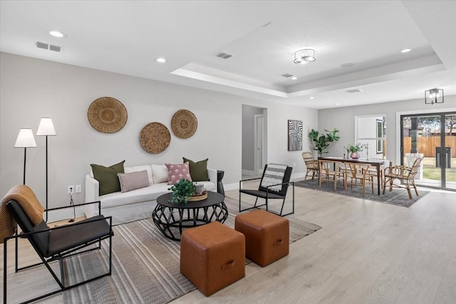 living room with light hardwood / wood-style floors and a tray ceiling