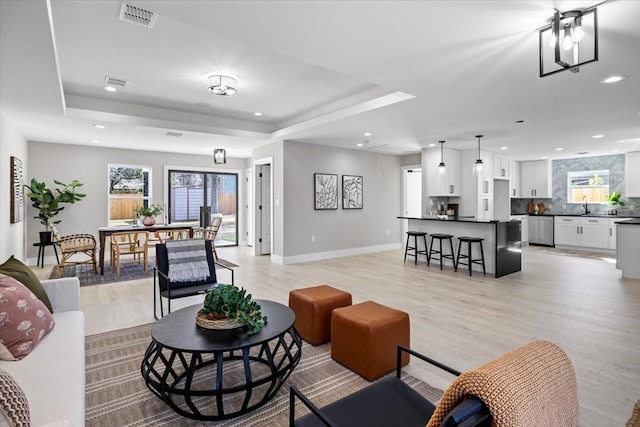 living room with light hardwood / wood-style floors, sink, and a tray ceiling