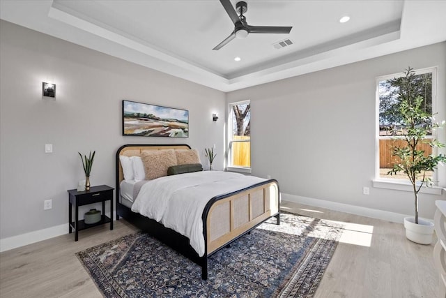 bedroom featuring ceiling fan, light hardwood / wood-style floors, and a raised ceiling