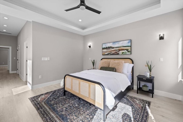 bedroom with ceiling fan, a tray ceiling, and light wood-type flooring