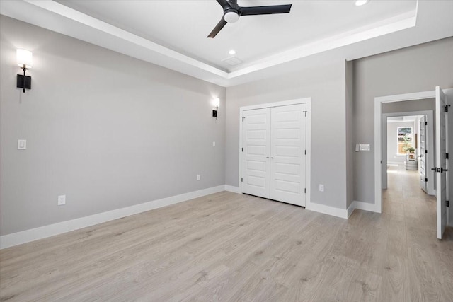 unfurnished bedroom featuring ceiling fan, light hardwood / wood-style flooring, a closet, and a tray ceiling