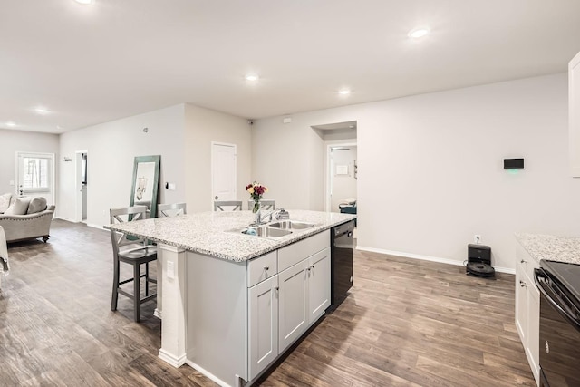 kitchen with sink, dark wood-type flooring, black appliances, light stone countertops, and a center island with sink