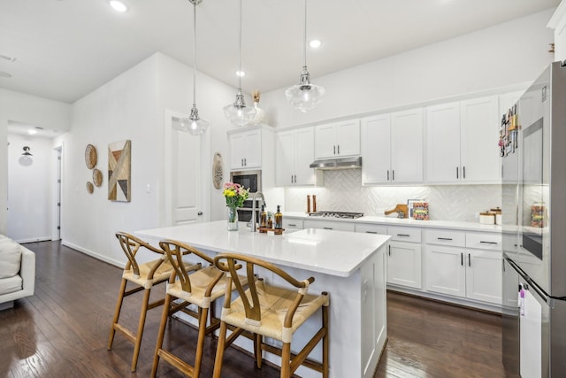 kitchen with stainless steel gas cooktop, white cabinetry, hanging light fixtures, black microwave, and a center island with sink