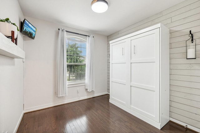 unfurnished bedroom featuring dark hardwood / wood-style floors, a closet, and wooden walls