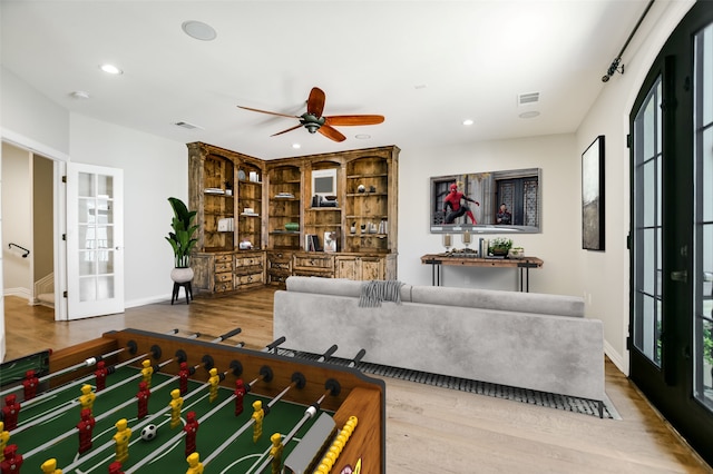 living room with wood-type flooring, built in shelves, ceiling fan, and french doors